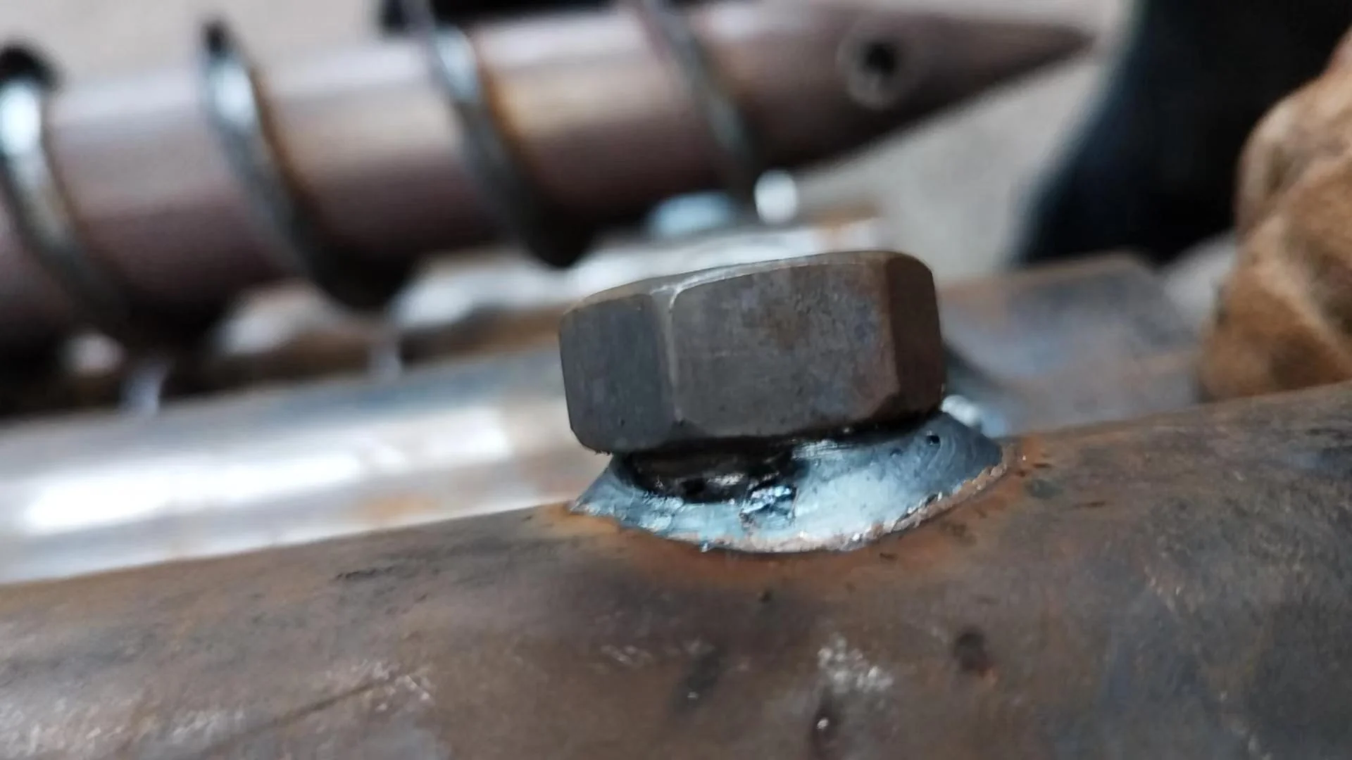 M16 nuts being welded onto the steel pipe, but quality issues arose, requiring Alexander Blasig and Xiaoshu Li to adjust the machinery.
