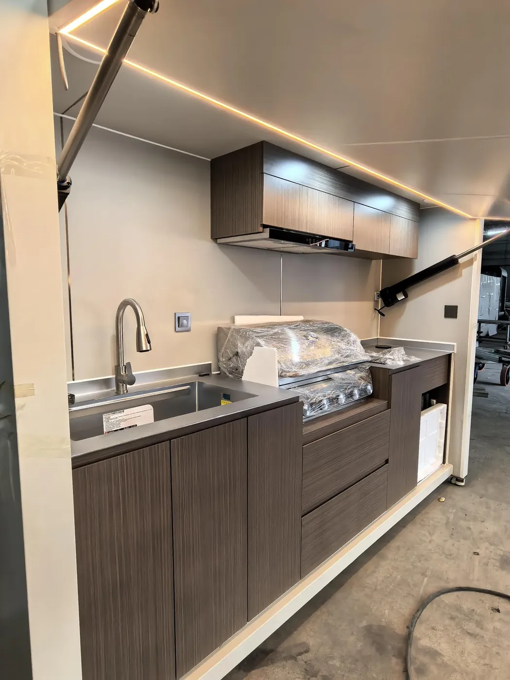 The ordered outdoor kitchen is completed. It includes a barbecue grill, induction cooktop, range hood, mini refrigerator, outdoor Bluetooth speaker, stainless steel worktop, wireless charging pad with power outlets, and more.